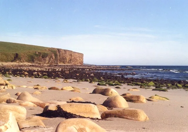 The sandy beach at Dingieshowe, Deerness, Orkney — pale sand scattered with sea-smoothed boulders below a low headland