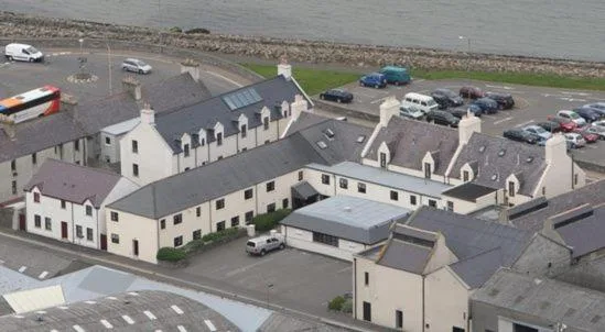 Ayre Hotel and Ayre Apartments on Ayre Road in Kirkwall, a long whitewashed seafront building with the Peerie Sea bay in the foreground and the slate roofs of Kirkwall behind