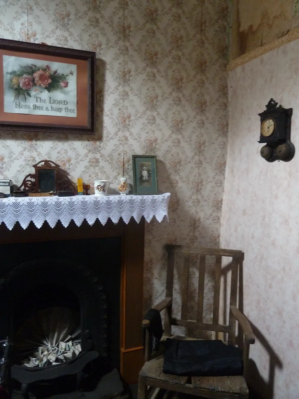 The parlour inside Kirbuster Farm Museum at Birsay, Orkney — papered walls, a cast-iron grate under a lace-edged mantel cloth, a wall clock and a wooden rocking chair