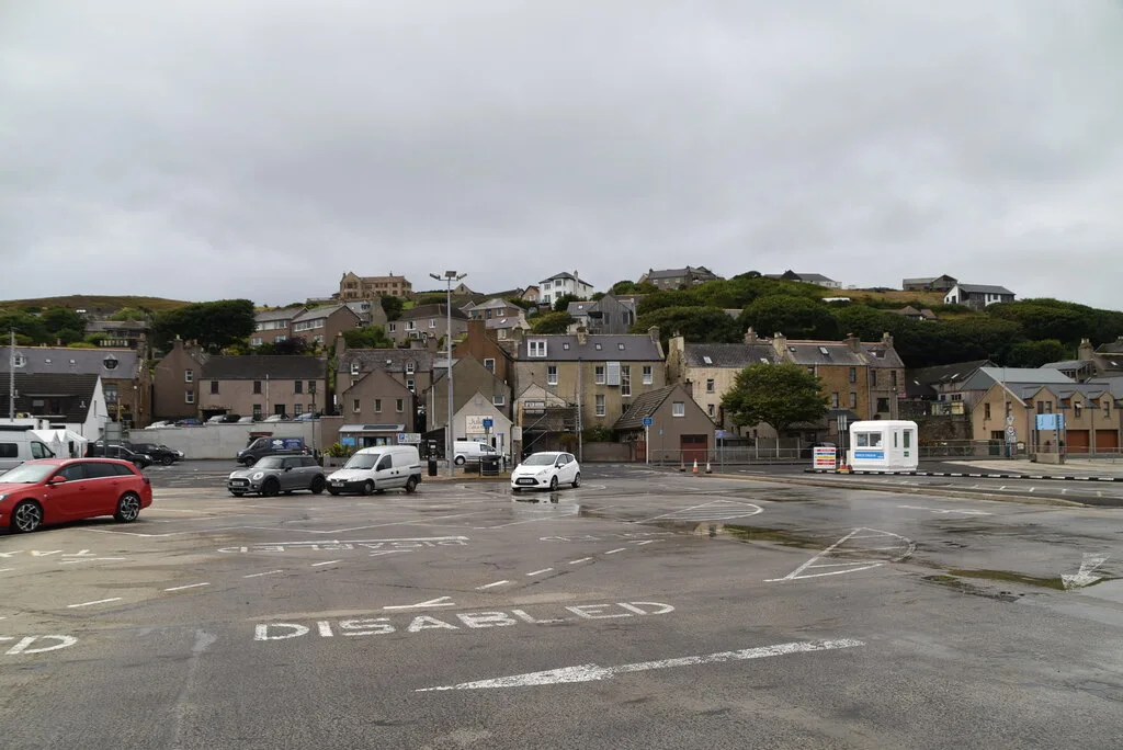The pay-and-display car park at Stromness Ferry Terminal with the town's stone houses behind