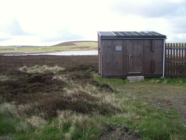The wooden bird hide beside Mill Loch on Eday, Orkney, with heather moorland around the freshwater loch under a cloudy sky.