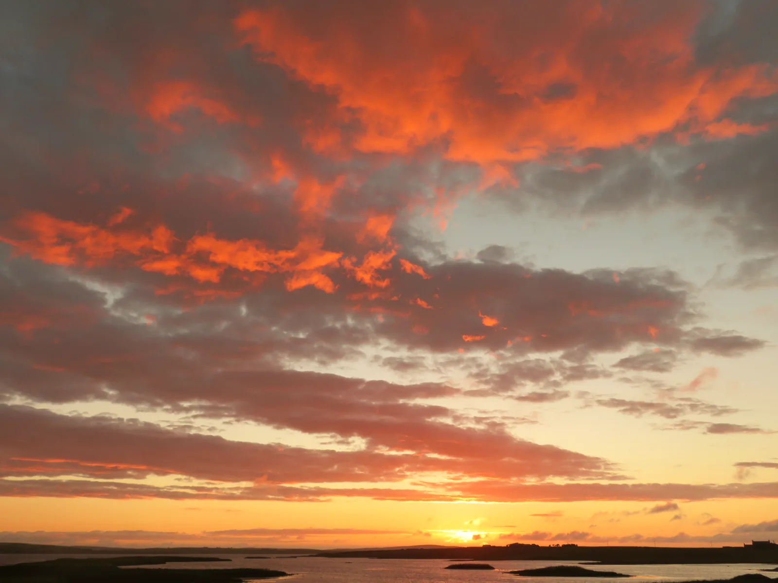 Fiery orange and red sunset sky over the calm water of the Loch of Harray in Orkney’s West Mainland