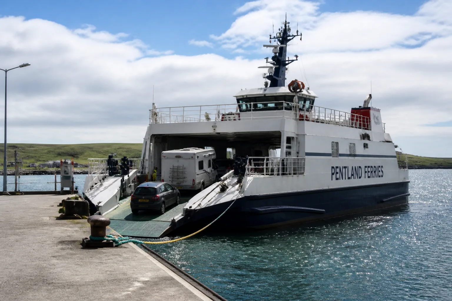 Pentland Ferries catamaran MV Alfred — distinctive twin-hulled white catamaran with tall navy-and-white superstructure — berthed at the small stone pier at St Margaret's Hope, South Ronaldsay, Orkney, on a partly-sunny summer afternoon with bow ramp down and a queue of cars loading