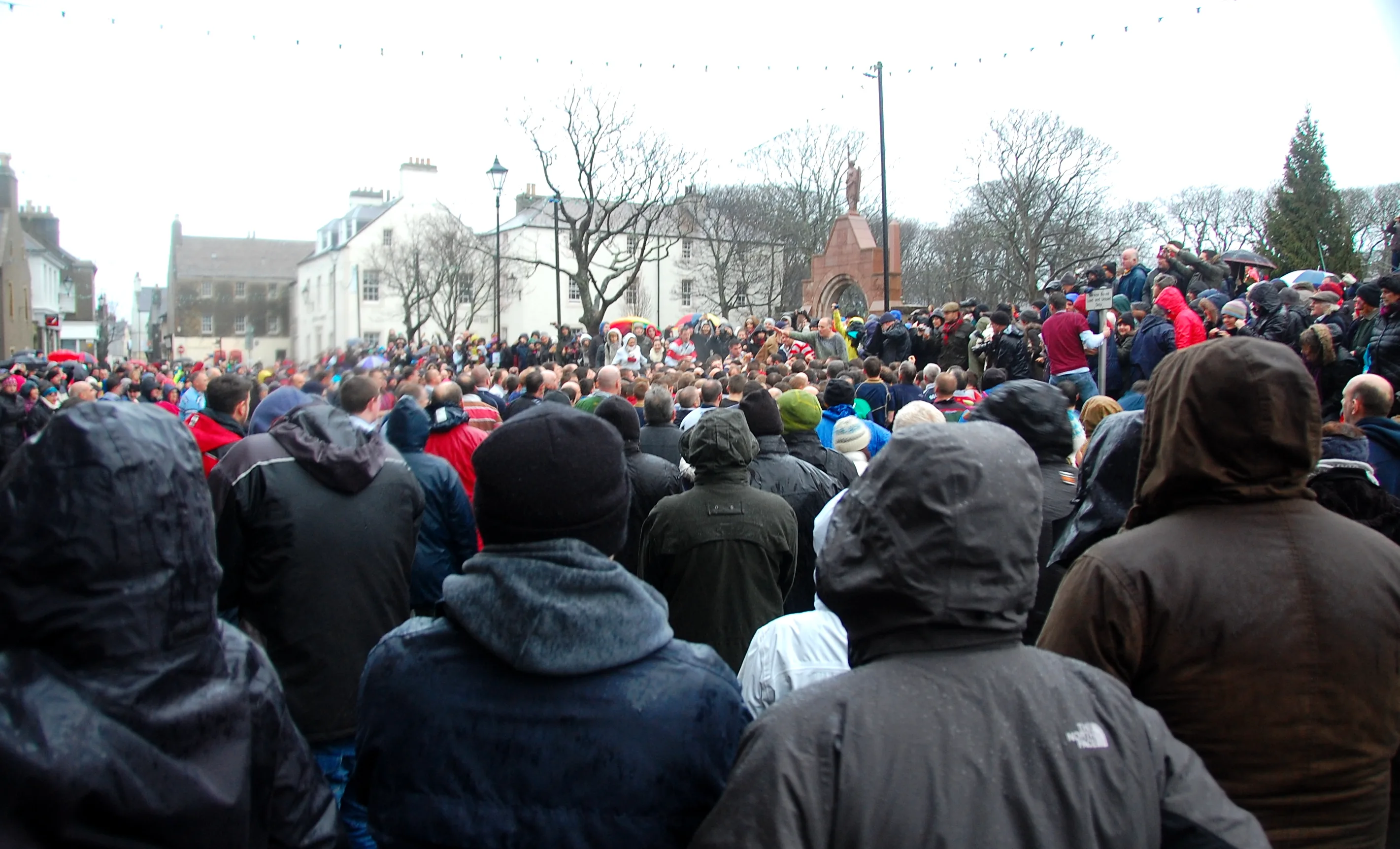 A large crowd of spectators in winter coats and hats gathered on Kirk Green in front of St Magnus Cathedral, Kirkwall, waiting for the Ba' to begin