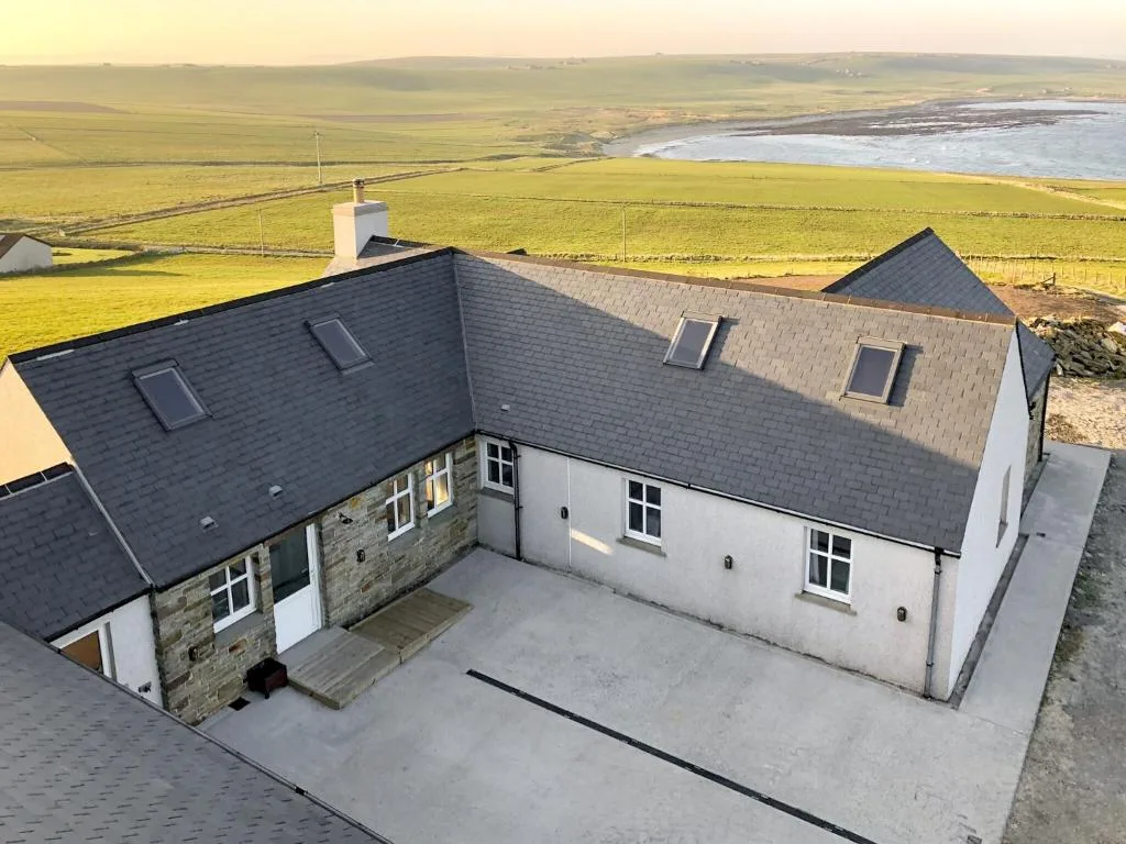 Egypt, a four-star coastal holiday home on the East Mainland of Orkney, seen from the air with an open sea bay directly behind the house across the fields