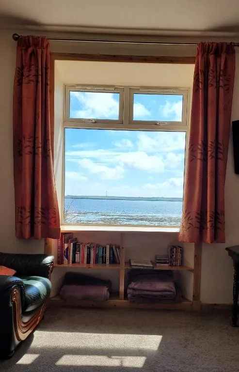 A lounge window at Glenduron-by-Sea at St Marys in Holm, Orkney, framing the open sea, with seals visible on the shoreline below the property
