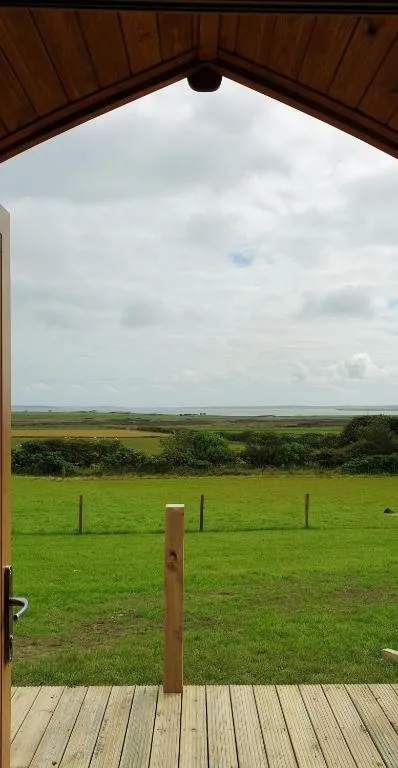 Lilly's Lodges Hedgehog Lodge near Finstown, Orkney, with open water and a passing ferry visible across the field from the lodge grounds