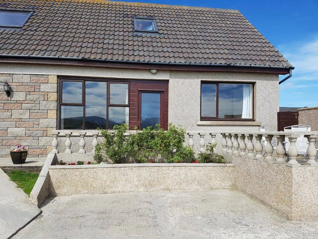 Lindisfarne Self-Catering, a ground-floor two-bedroom apartment at Navershaw near Stromness, with private outdoor dining area facing the bay and the Hoy hills in the background