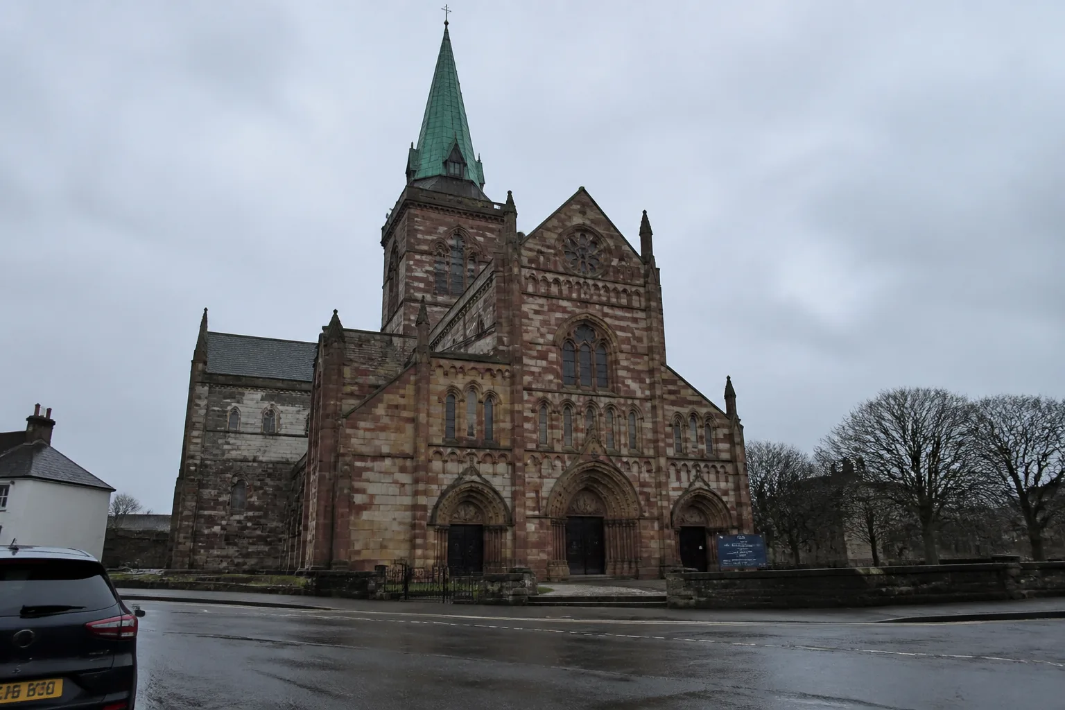 St Magnus Cathedral on Broad Street, Kirkwall — the distinctive red-and-yellow chequerboard sandstone Romanesque west front with the tall copper-clad spire added in 1908