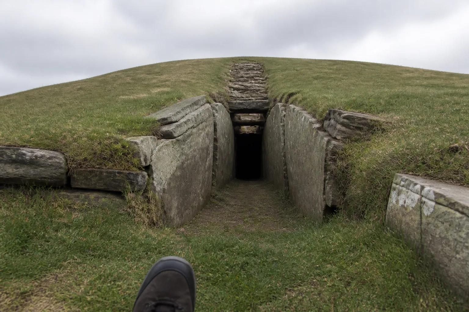 Low stone entrance passage of Maeshowe chambered tomb, Orkney — narrow rectangular passage made of huge flat slabs of grey sandstone leading into darkness inside the green grass-covered burial mound