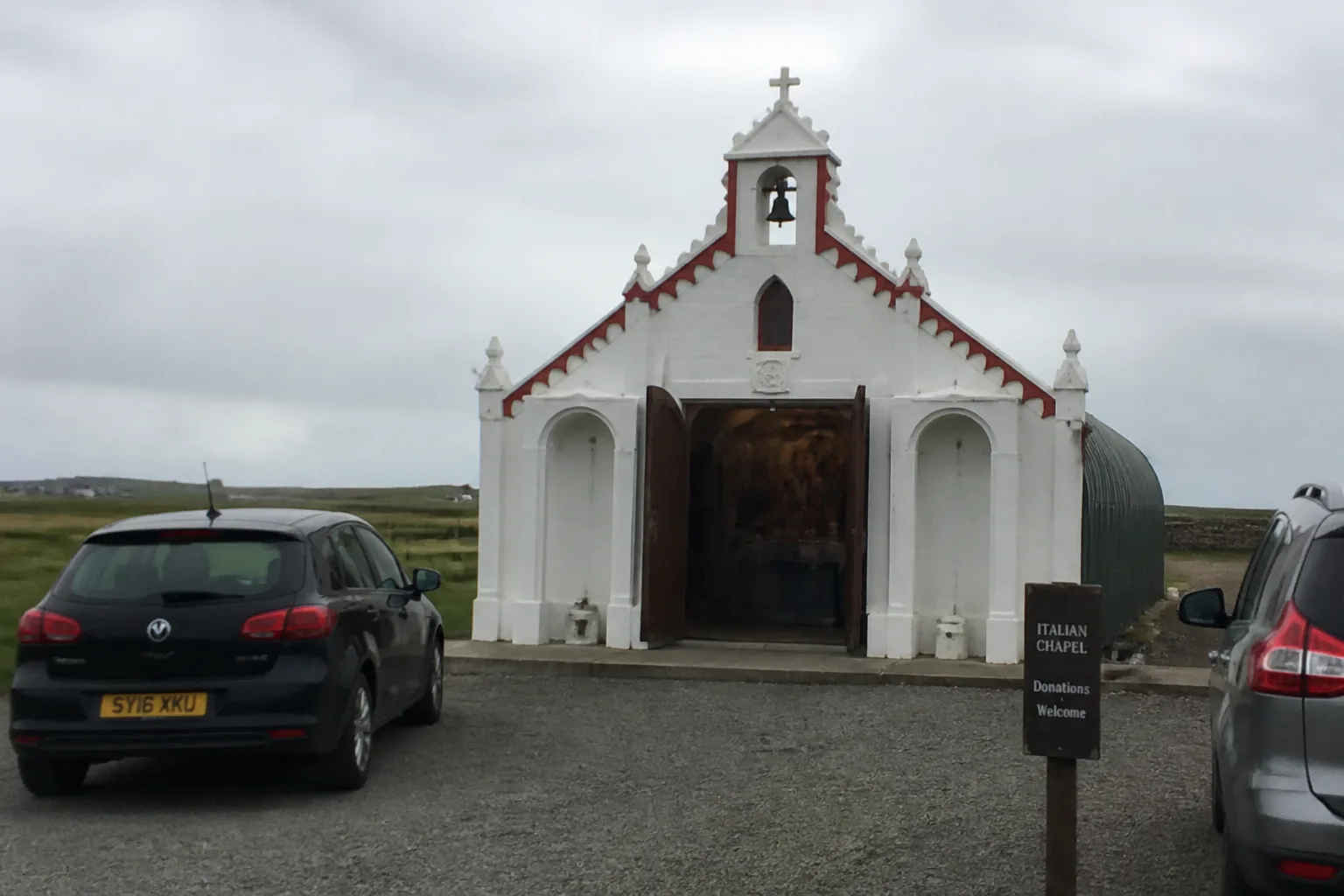 The Italian Chapel exterior on Lamb Holm, Orkney — small white-painted concrete façade built by WWII Italian POWs from two corrugated Nissen huts, with classical archways flanking the entrance and a small bell tower