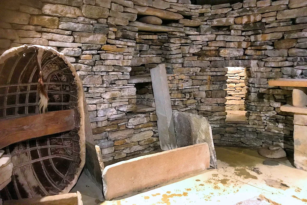Interior of the full-scale reconstructed replica of House 7 at Skara Brae, showing a stone dresser, stone box-bed frames and a central hearth stone inside a circular drystone chamber