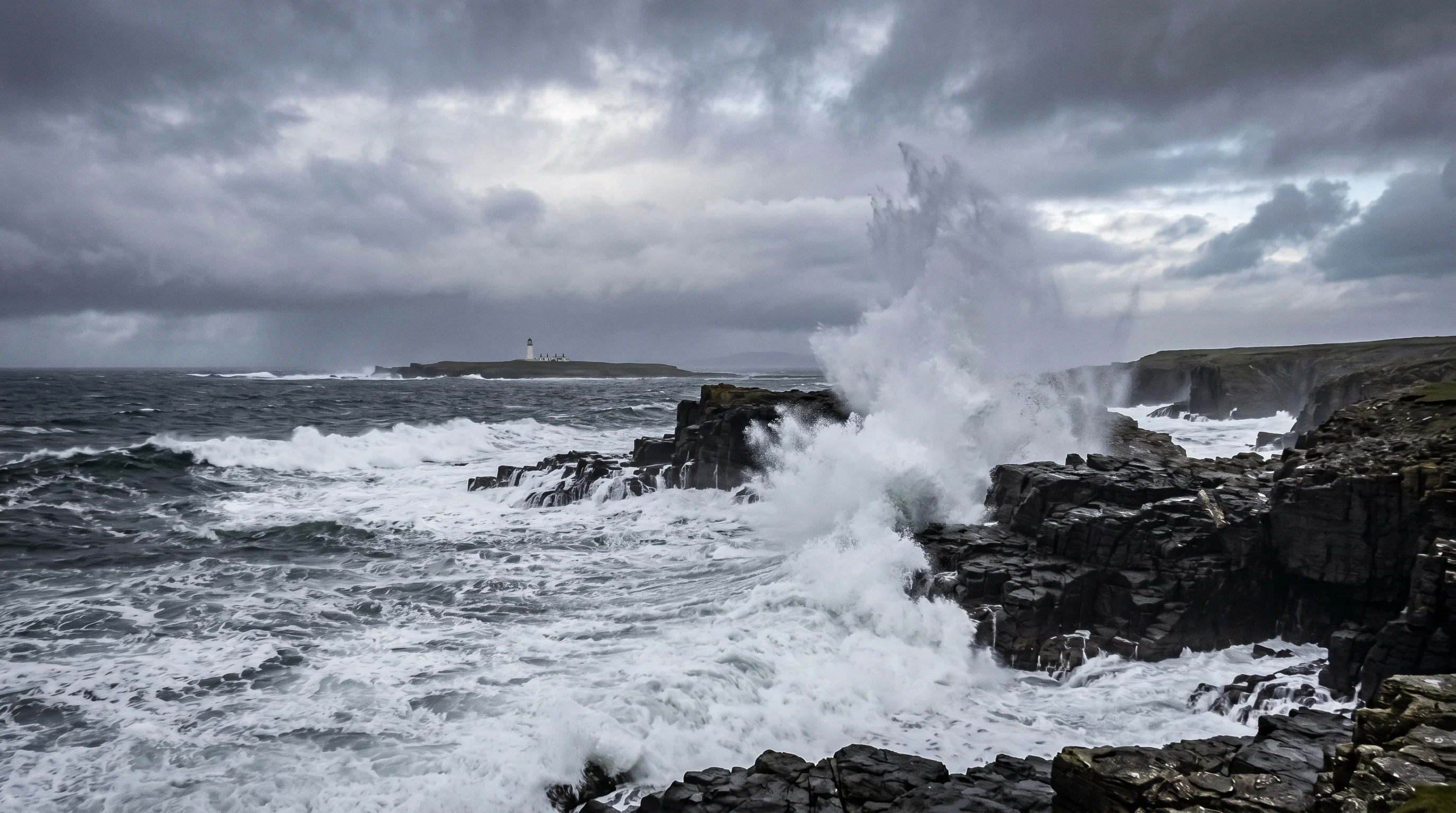 Huge white-capped Atlantic waves smashing into the dark basalt rocks below Birsay Bay, Orkney, during an October gale, with the lighthouse just visible through low cloud