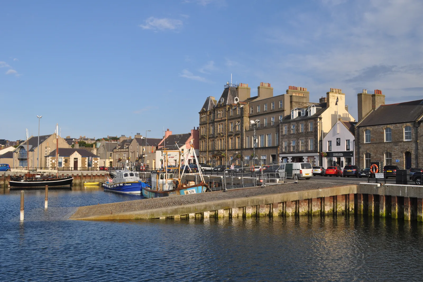 Kirkwall harbour on a clear day, fishing boats moored against the pier with the waterfront buildings of the town behind