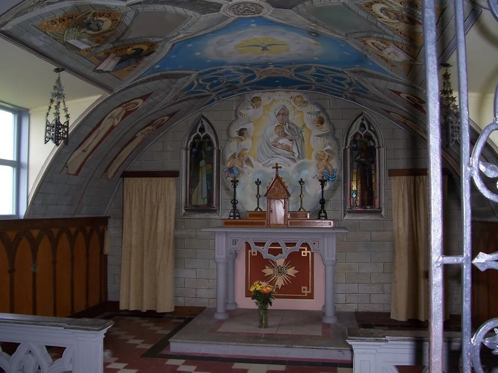 The painted interior of the Italian Chapel on Lamb Holm, showing the vaulted ceiling and altar decorated to look like carved stone and brickwork.