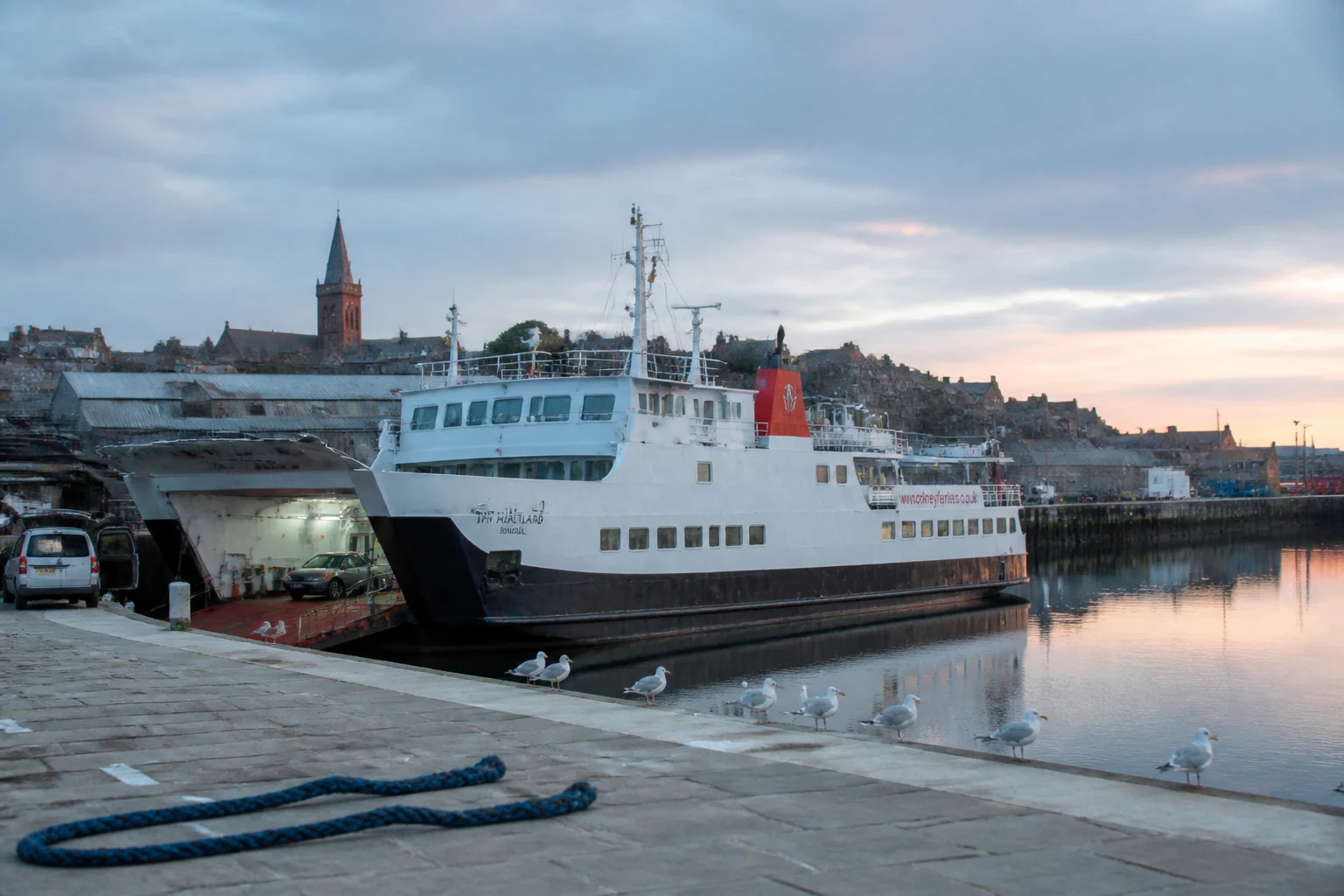 Kirkwall harbour at first light at five thirty in the morning in mid-June with the MV Hjaltland inter-island ferry moored at the pier and the red sandstone tower of St Magnus Cathedral catching first sunlight in the background