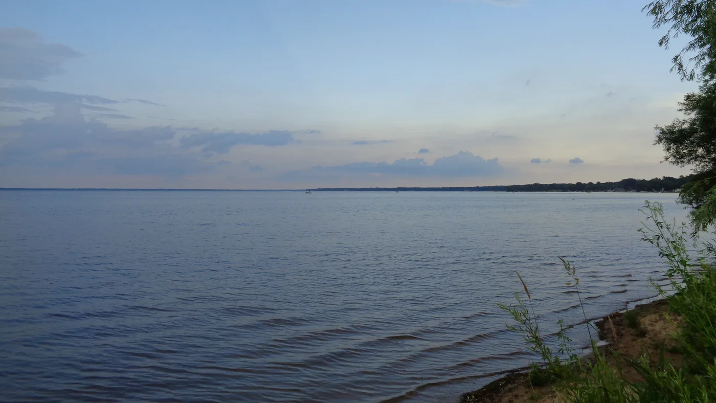 Panoramic view of Houghton Lake, Michigan on a summer evening showing the vast expanse of calm water stretching to the distant pine-forested shoreline