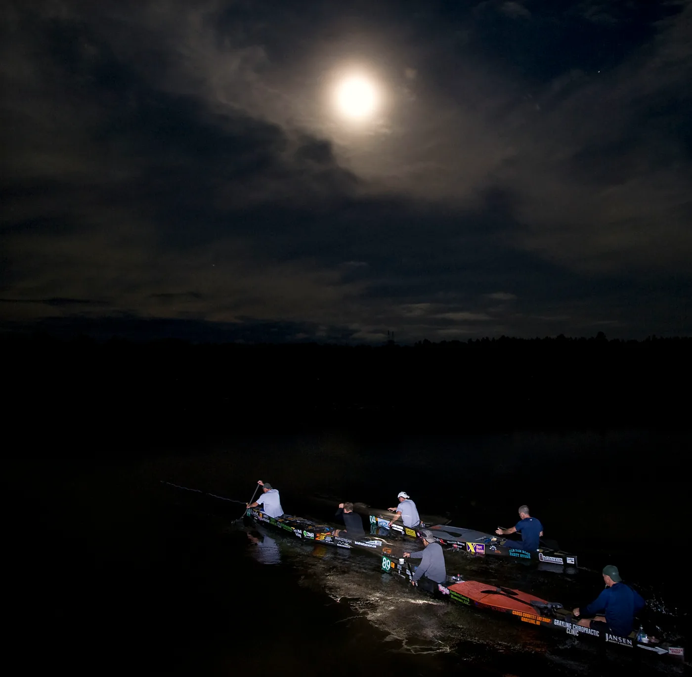 Canoes racing across Mio Pond under moonlight during the Au Sable River Canoe Marathon in Michigan