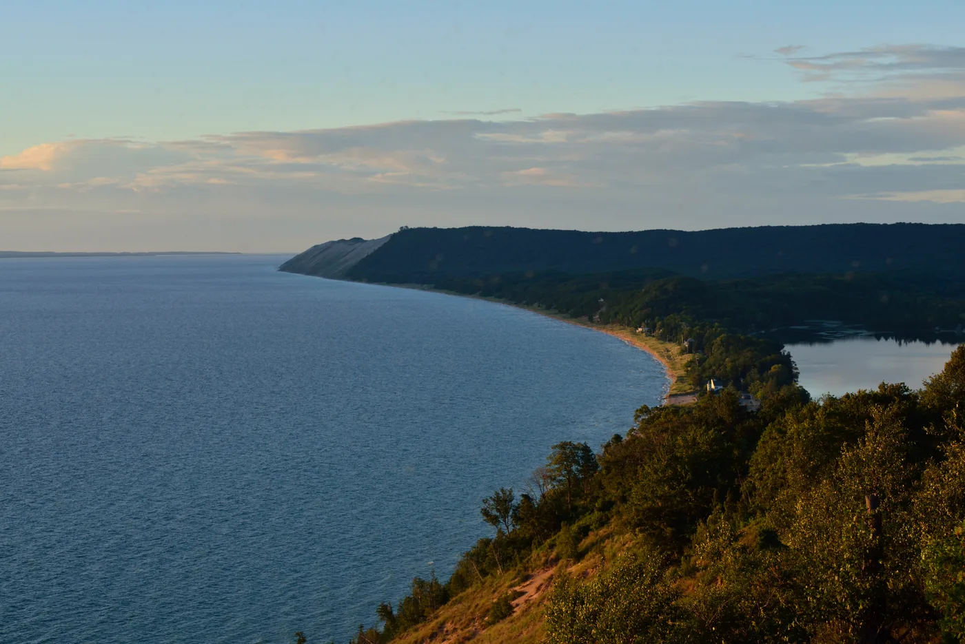Evening view from the Empire Bluffs Trail overlook, the Lake Michigan shoreline curving north below forested bluffs toward the Sleeping Bear plateau