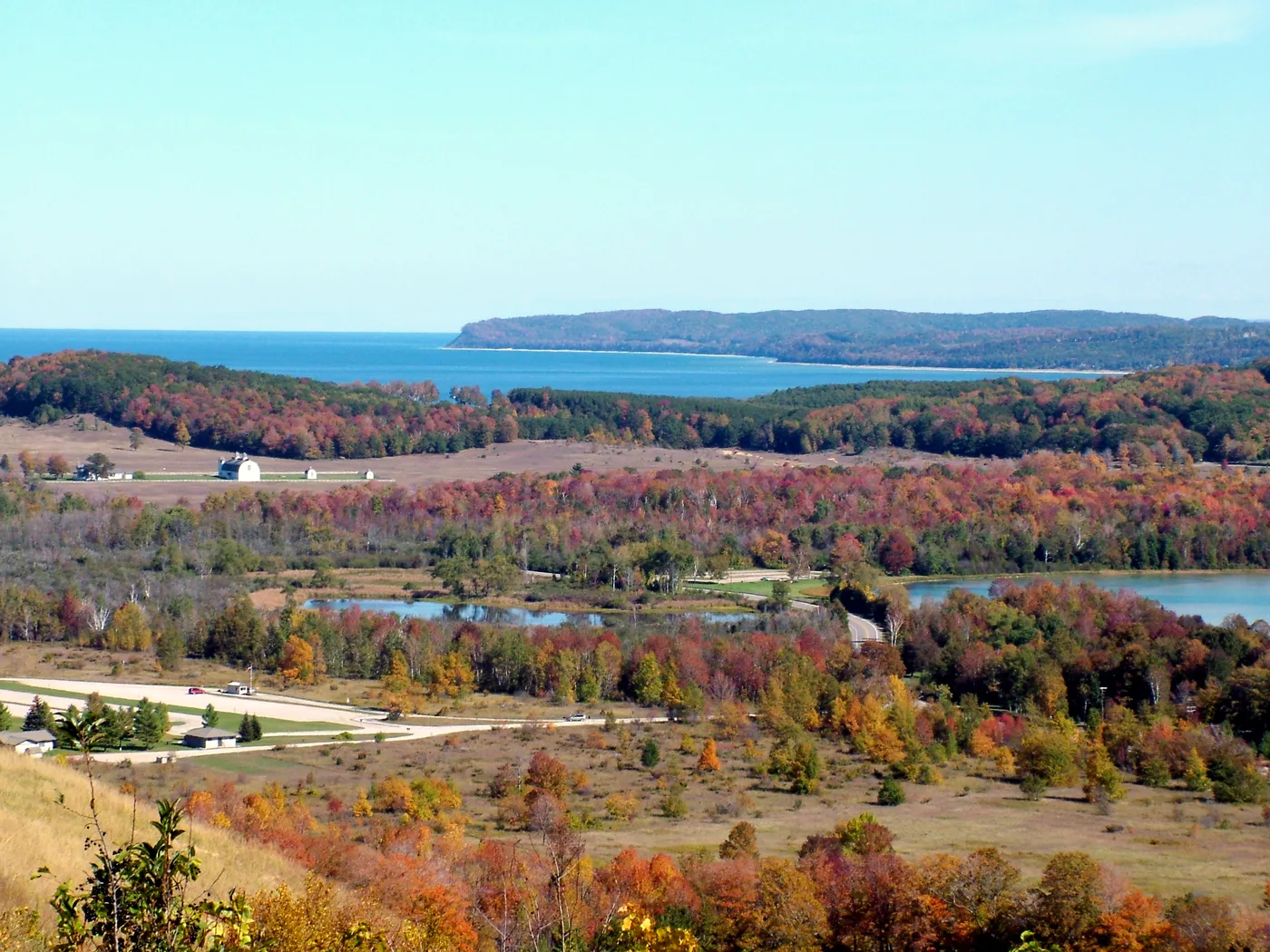 Peak fall color across the Glen Lakes in Sleeping Bear Dunes National Lakeshore, red and orange hardwoods running down to the water with Lake Michigan beyond