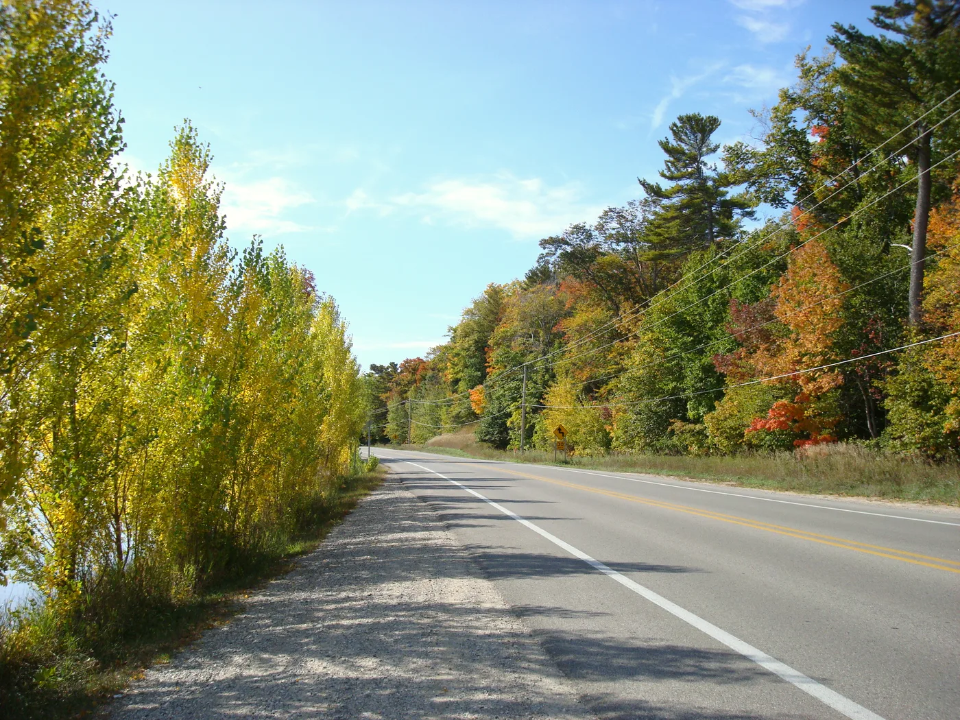 Fall color along M-22 on the Leelanau Peninsula, yellow and orange maples lining both sides of the two-lane highway under a blue sky