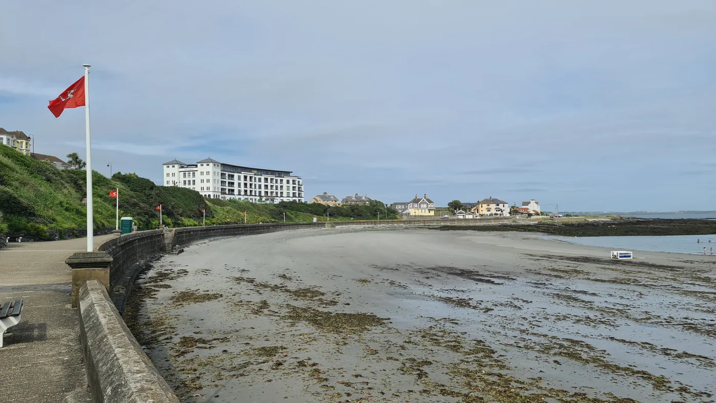 The sandy beach at Chapel Bay in Port St Mary, curving below a promenade wall and a Manx flag at low tide