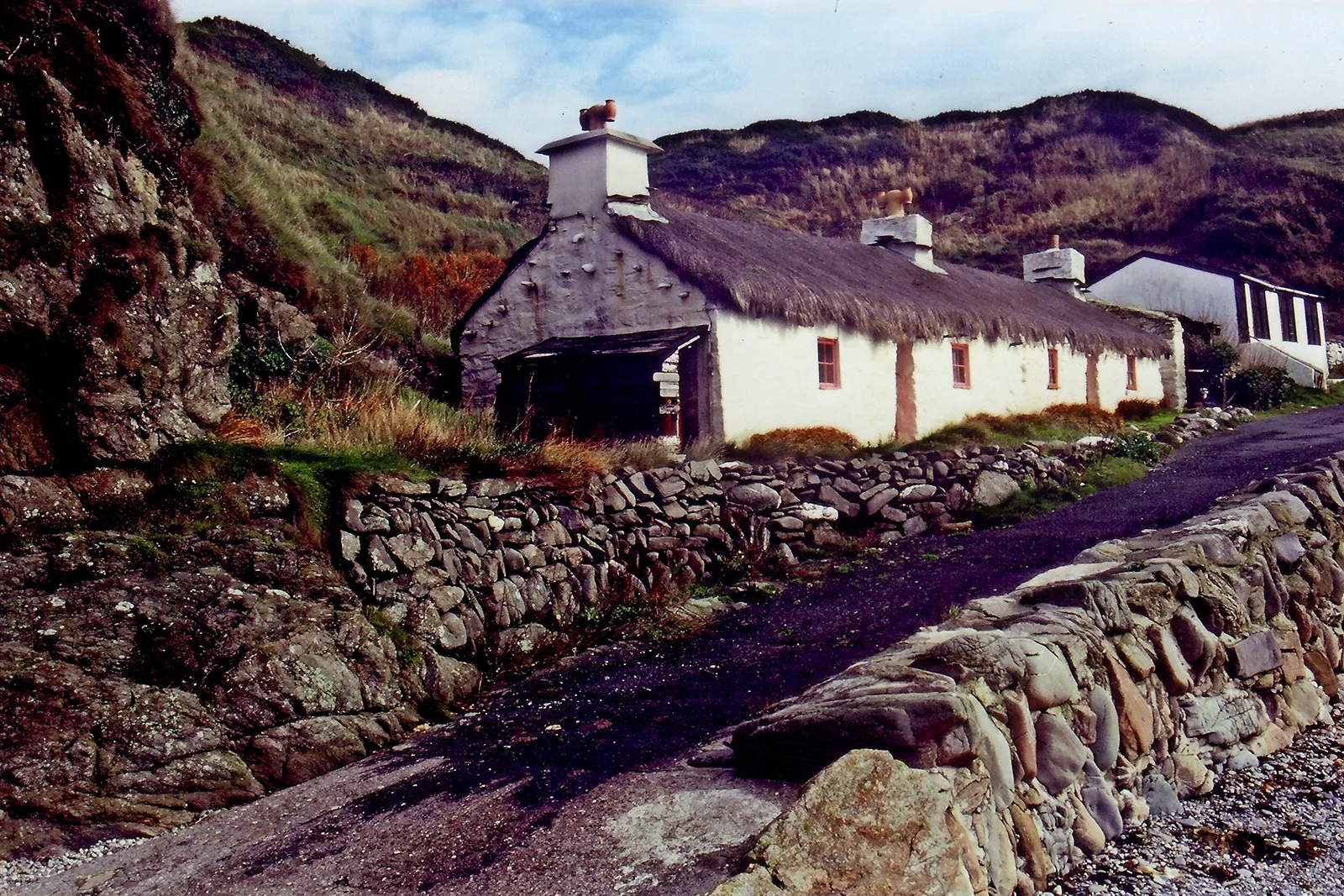 A whitewashed thatched cottage behind a stone wall on the lane at Niarbyl