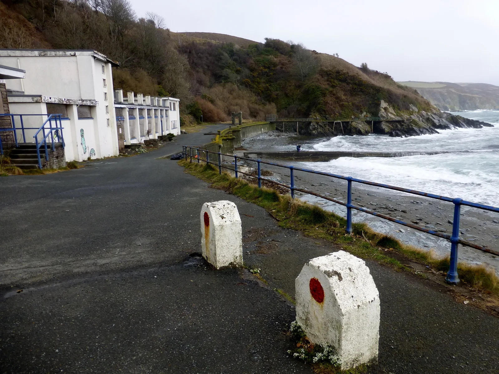 Shuttered white buildings beside the shingle shore and sea wall at Port Soderick