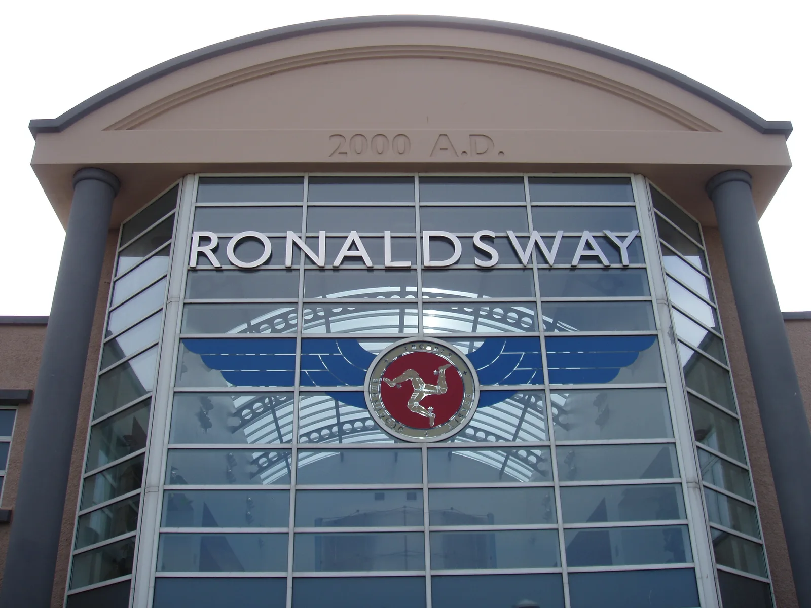 The glazed front of the passenger terminal at Ronaldsway Airport, with the name above a three-legged Manx emblem