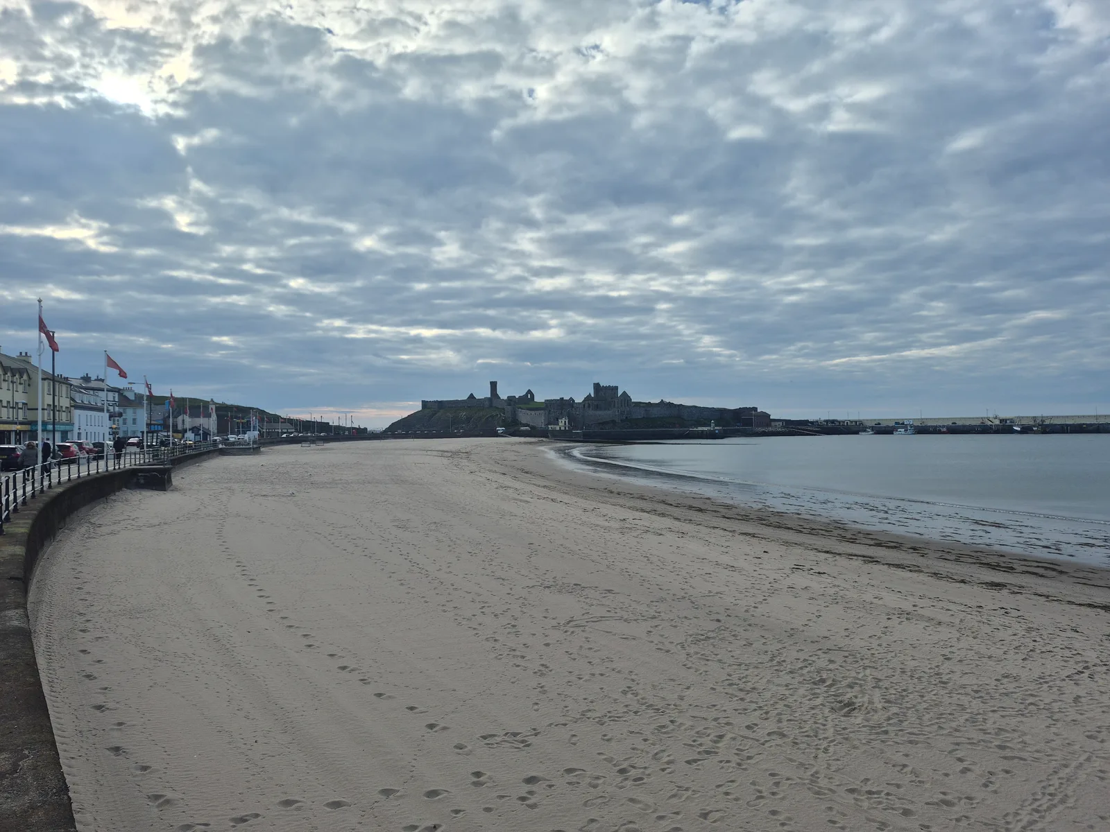 The curving sand of Peel beach below the promenade, with Peel Castle at the far end