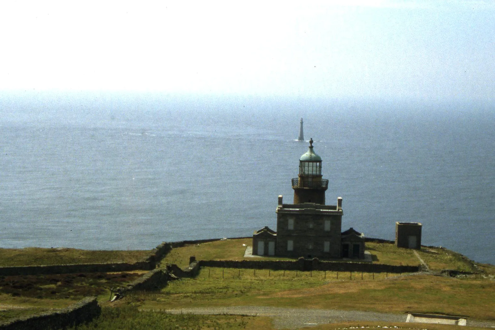 The disused lower lighthouse on the Calf of Man in the foreground, with the Chicken Rock lighthouse standing out at sea beyond