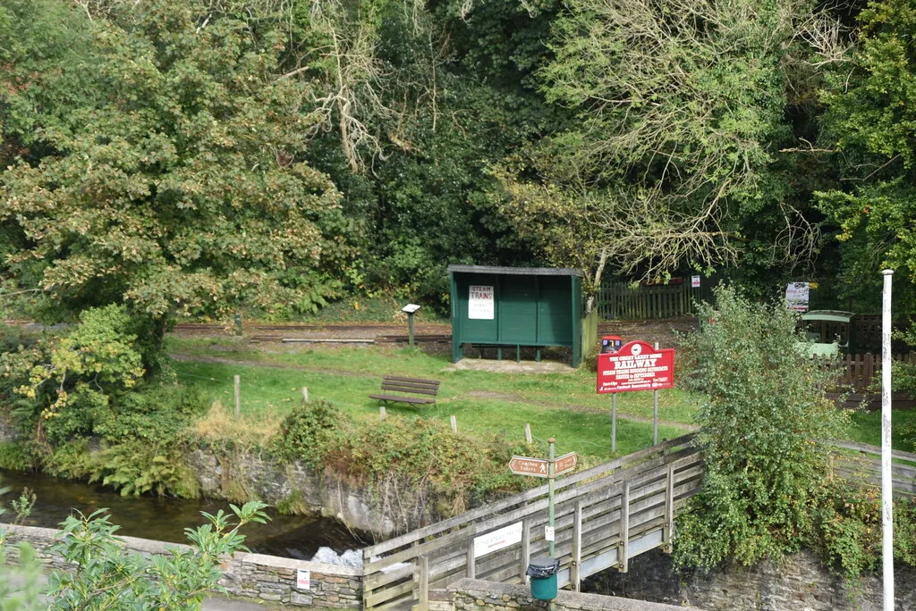A green passenger shelter and red Great Laxey Mine Railway sign beside the narrow-gauge line, reached by a footbridge