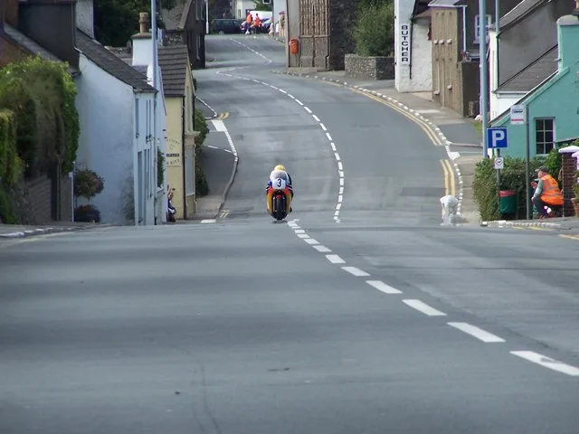 A motorcycle racing through Kirkmichael village during the Junior Classic Manx Grand Prix, spectators lining the street
