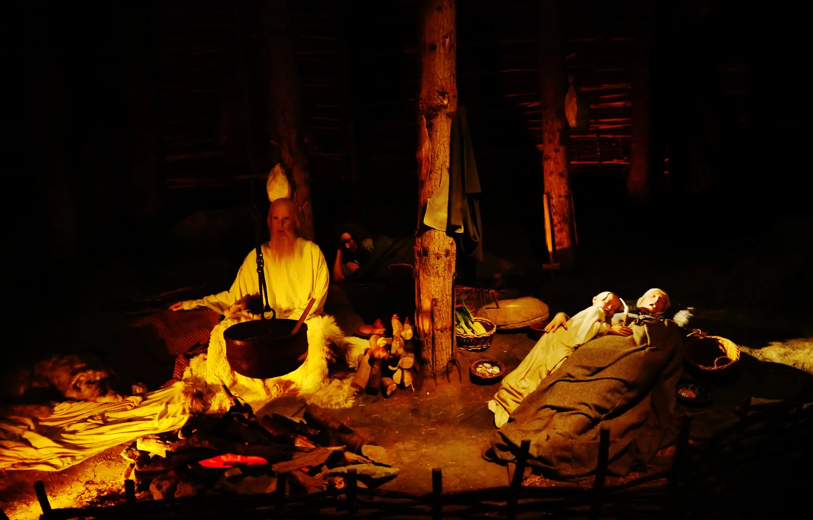 A dimly lit reconstruction inside the House of Manannan, with figures around a cooking pot over a hearth