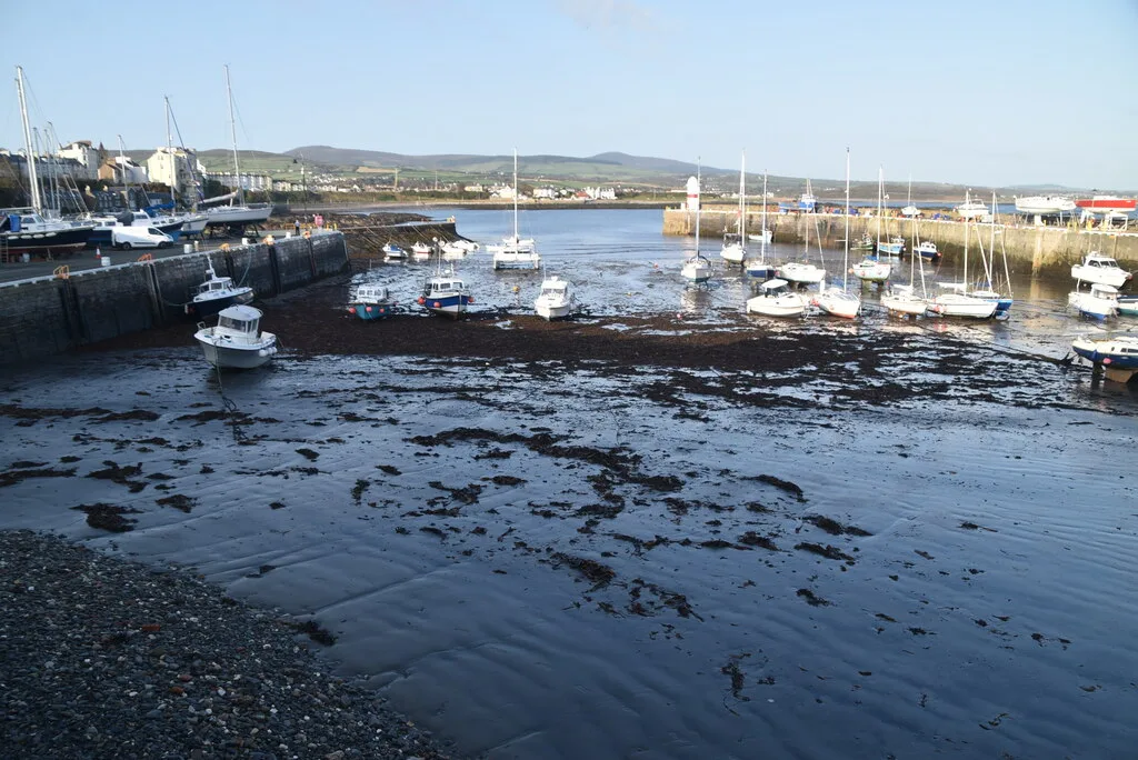 Small boats resting on the sand of Port St Mary harbour at low tide, with the breakwater and hills beyond