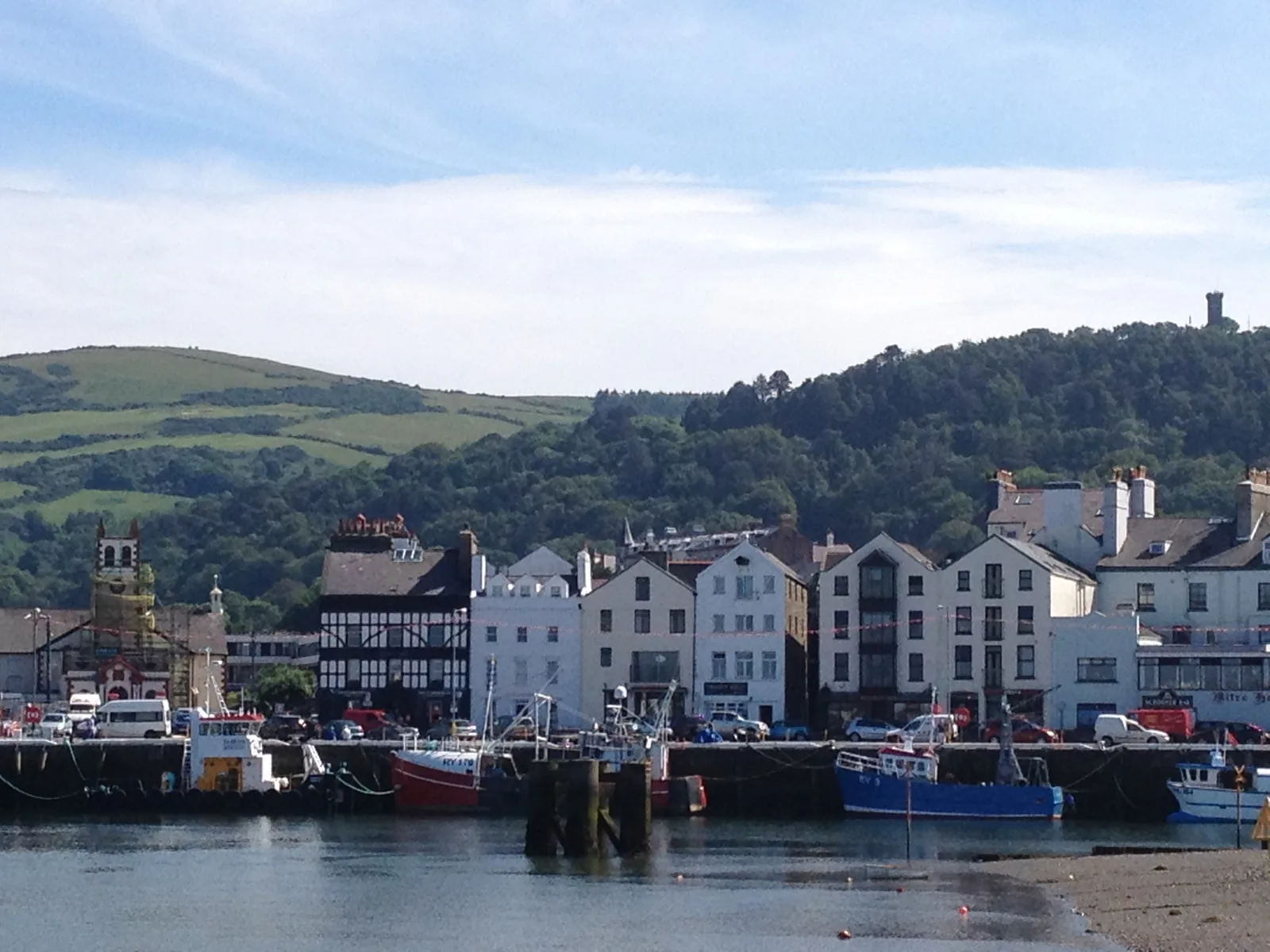 Fishing boats moored along the quay in Ramsey harbour, with the town and wooded hills behind