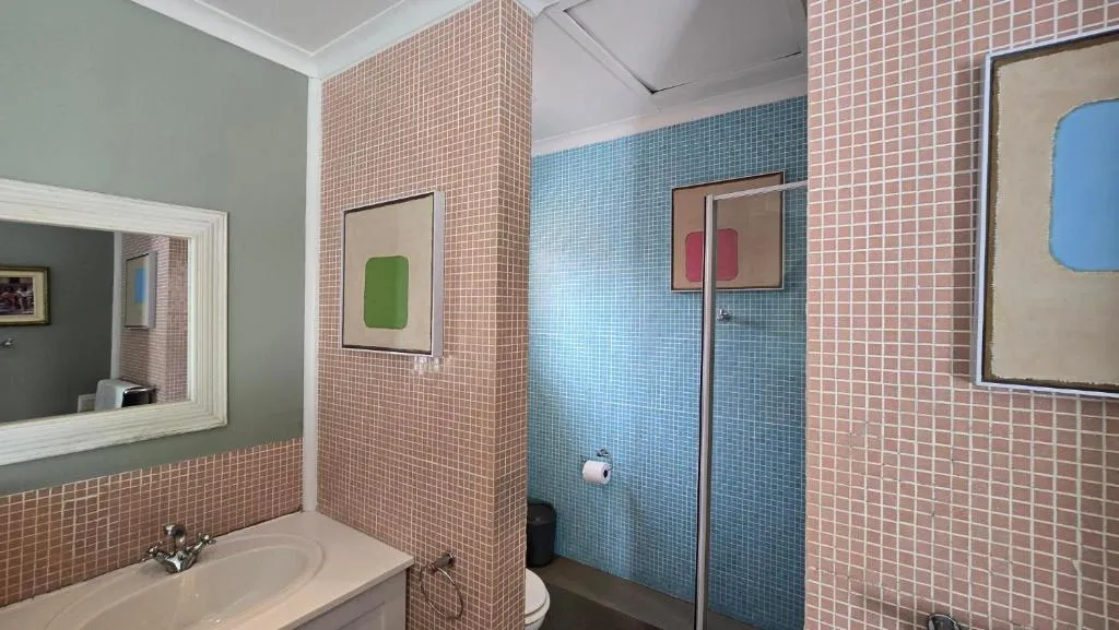 Bathroom with pink and blue mosaic tile, shower and pedestal-style vanity