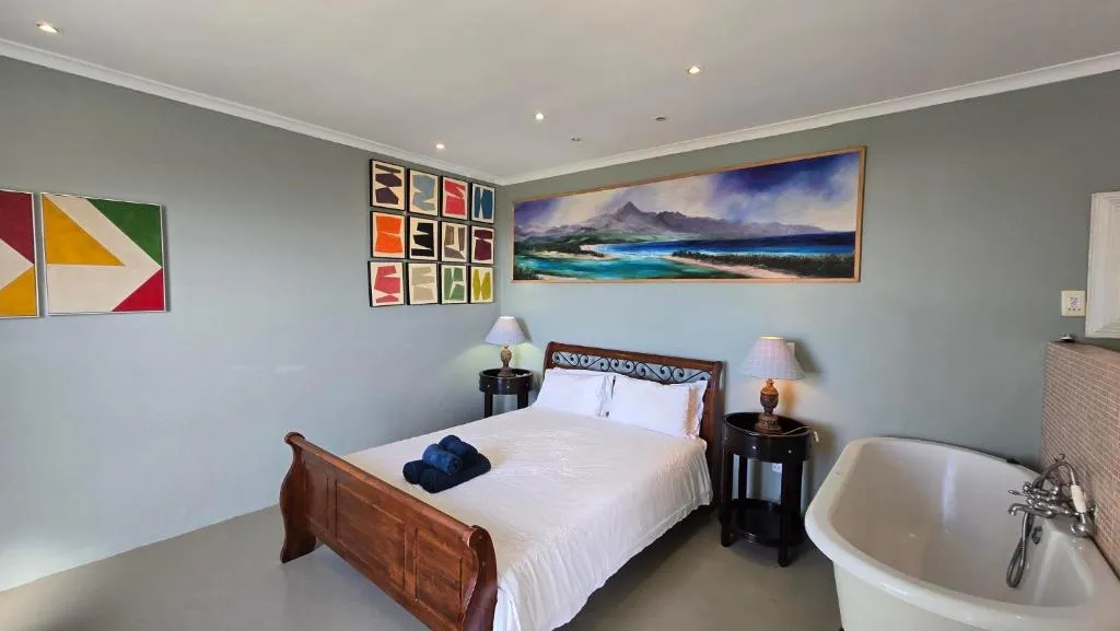 Bedroom with a wooden sleigh bed, freestanding tub and bold geometric wall art