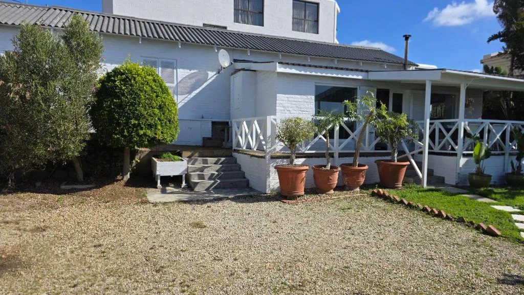 White house exterior with a gravel courtyard, potted plants and steps up to the veranda
