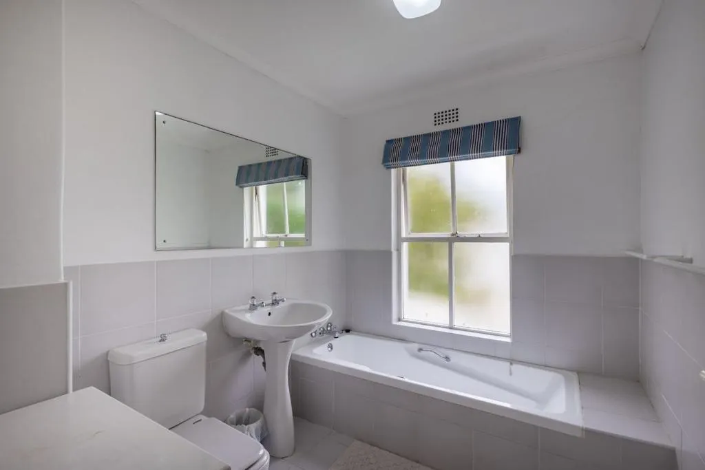 Bathroom with a pedestal sink, built-in tub, and a frosted window