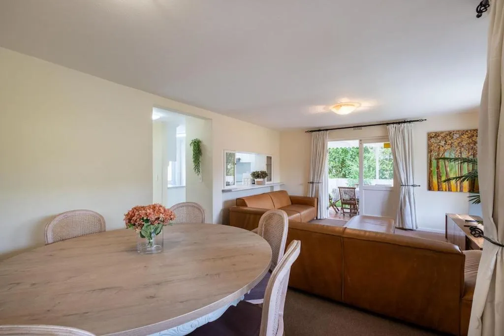 Dining table set for six beside a leather-sofa living area opening onto a covered porch