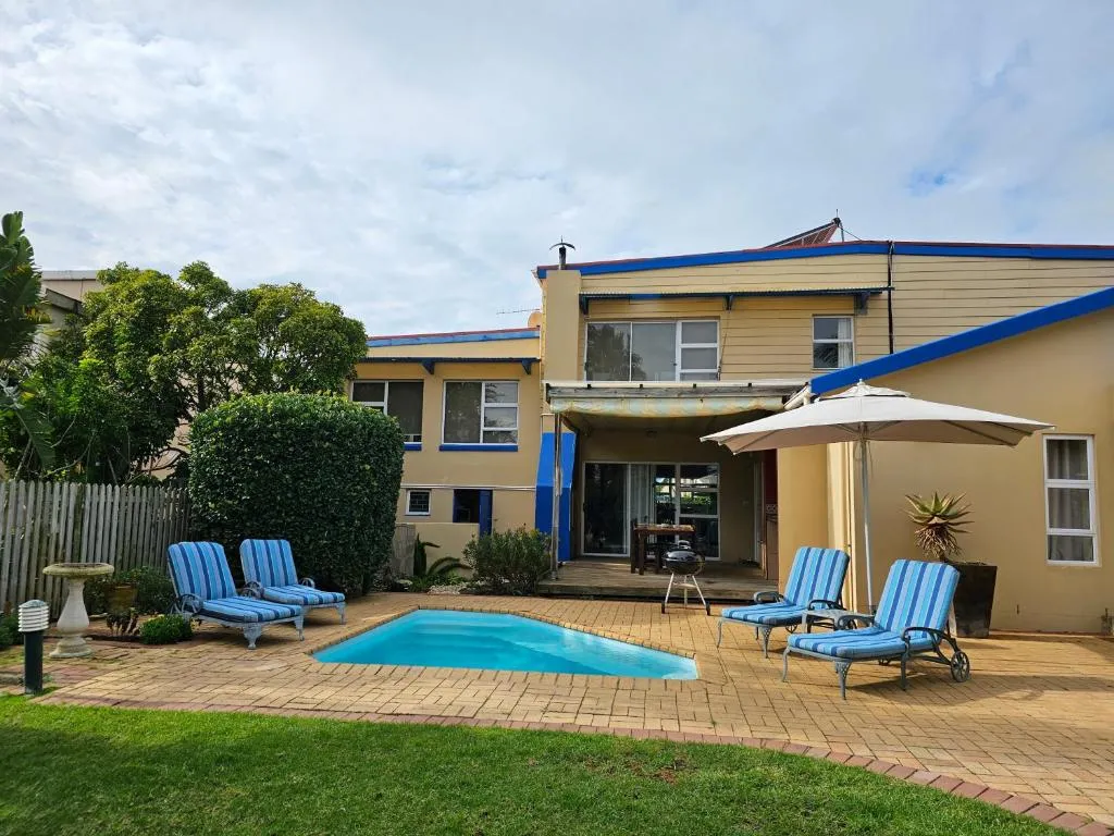 Guest house exterior with a paved pool, striped loungers and a braai under an umbrella