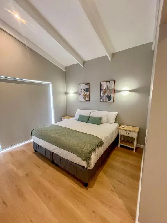 Bedroom with a vaulted beamed ceiling, wall sconces and a green throw over a double bed
