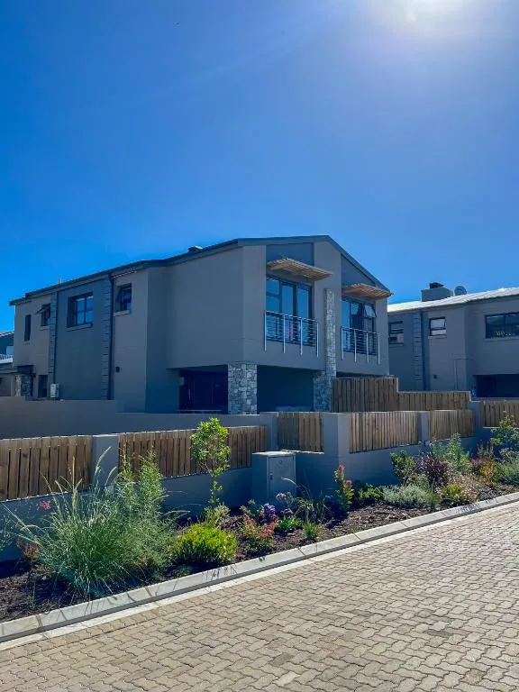 Two-storey grey townhouse with a stone-clad entrance and balcony in a modern estate street