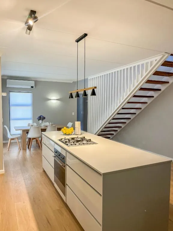 Kitchen island with a gas hob and built-in oven beside a staircase to the upper floor