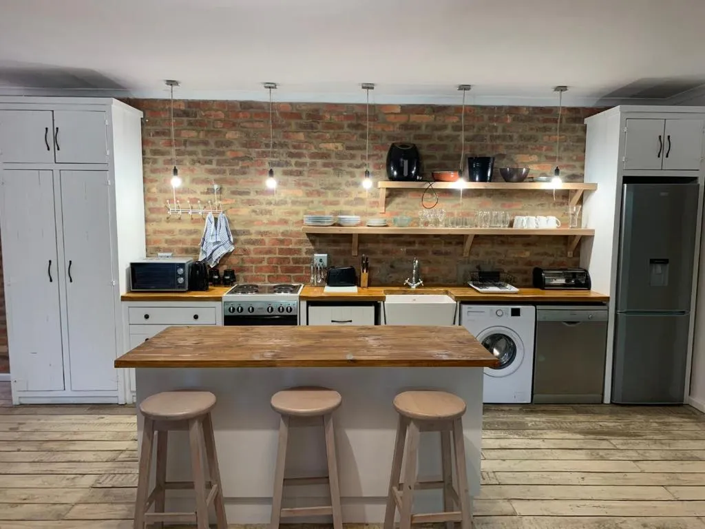 Farmhouse kitchen with gas stove, washing machine and open shelving on a brick wall