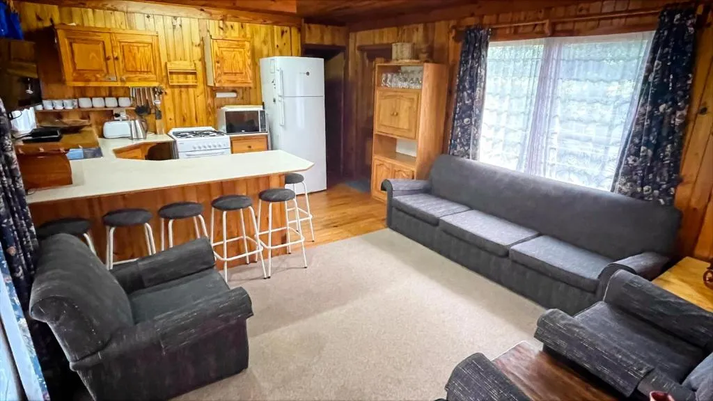 Open-plan pine-panelled kitchen with breakfast bar stools and lounge seating