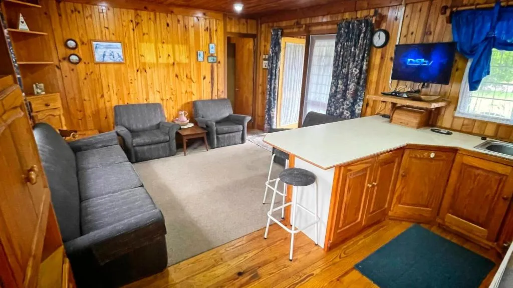 Pine-panelled lounge with grey sofas, armchairs and wall-mounted TV