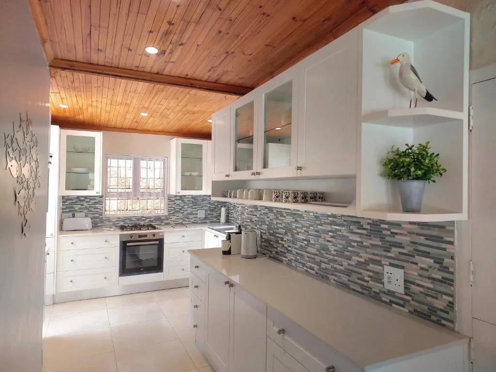 White kitchen with a mosaic tile backsplash, gas hob, and a wood-panelled ceiling