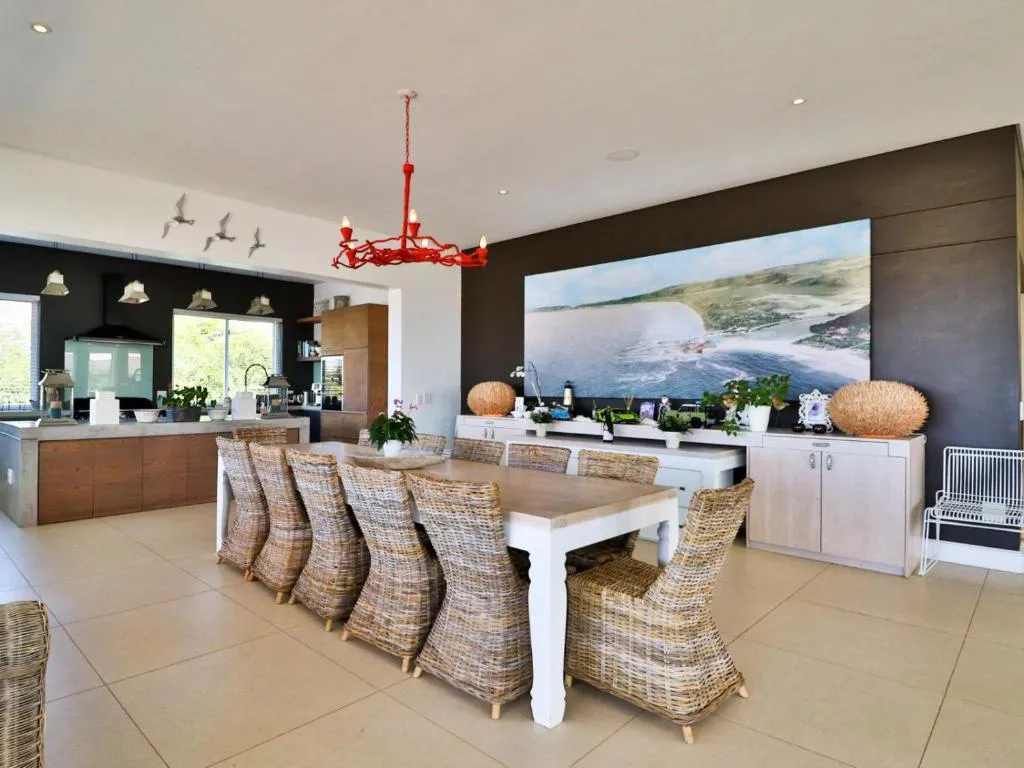 Open-plan dining table seating ten beneath a red pendant light, kitchen visible behind